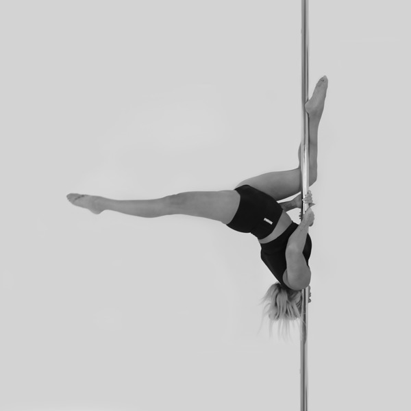 One woman holding a butterfly shouldermount pose during a pole fitness class at The Pole Hub