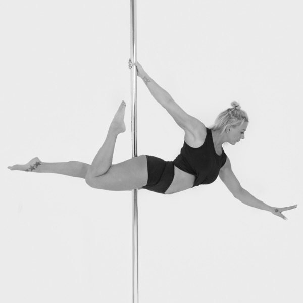 One woman holding a superman pose during a pole fitness class at The Pole Hub