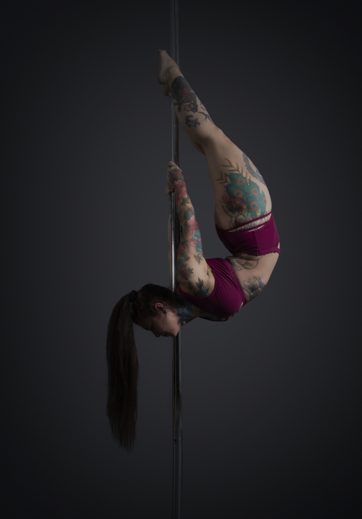One woman holding a pose during a pole fitness class at The Pole Hub